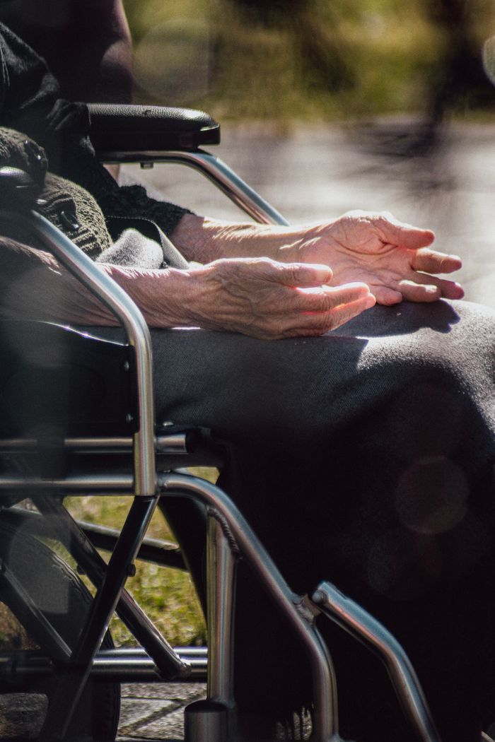 Close-up of elderly person's hands while sitting in a wheelchair outdoors.