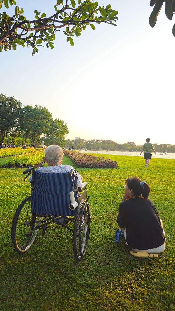 Elderly person and caregiver enjoy a serene afternoon by the river in Bangkok.