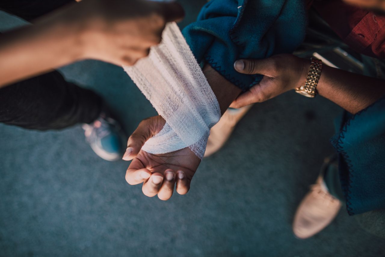A detail shot showing hands applying a bandage to an injured wrist outdoors.
